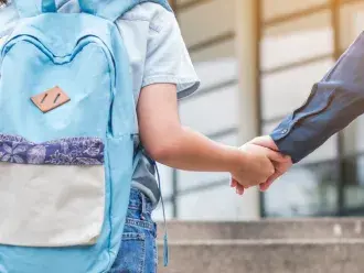 A child holds hands with a parent while walking to school.