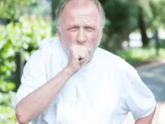 Elderly man coughs while outside on a walk.