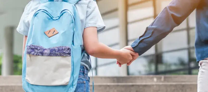 A child holds hands with a parent while walking to school.