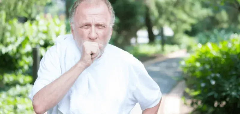 Elderly man coughs while outside on a walk.