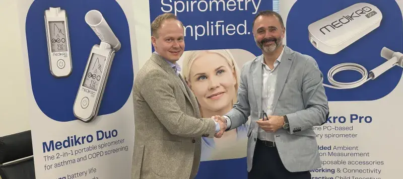 Two men shake hands in front of a product display.