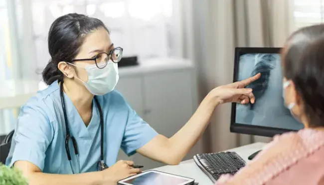 nurse with mask points to an x-ray of the lung