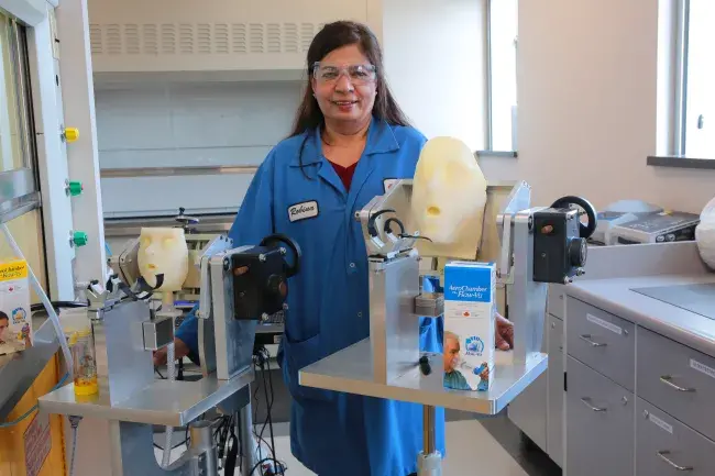 a woman in a lab coat stands with lab equipment.