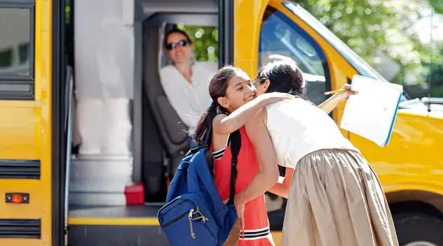 A child hugs her mom by a waiting bus.