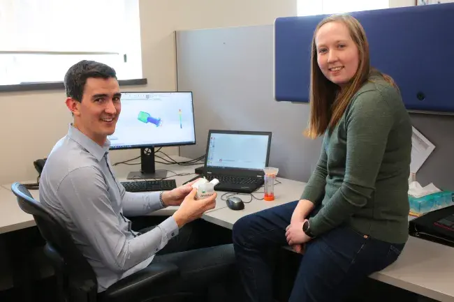 Two employees stand in front of a computer.