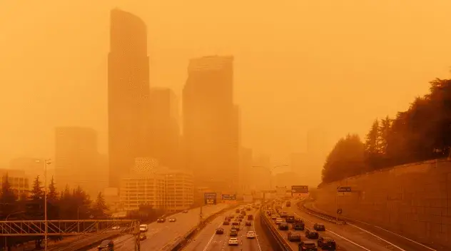 Wildfire smoke turns the sky orange over a highway through a city.